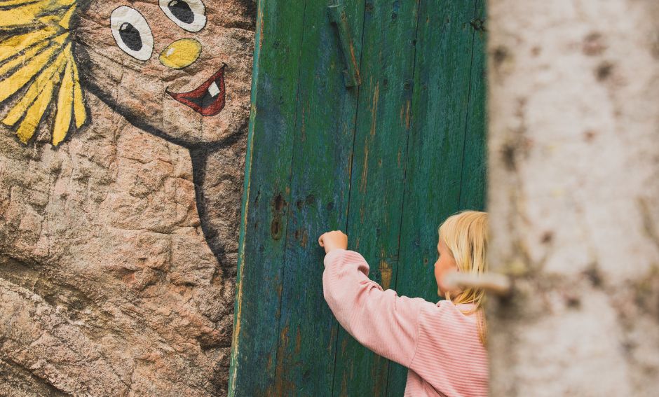 Flicka som knackar på grön dörr med målat troll på bergsvägg